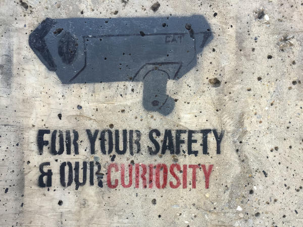 Graffiti of a camera with the message reading - For your safety and our curiosity